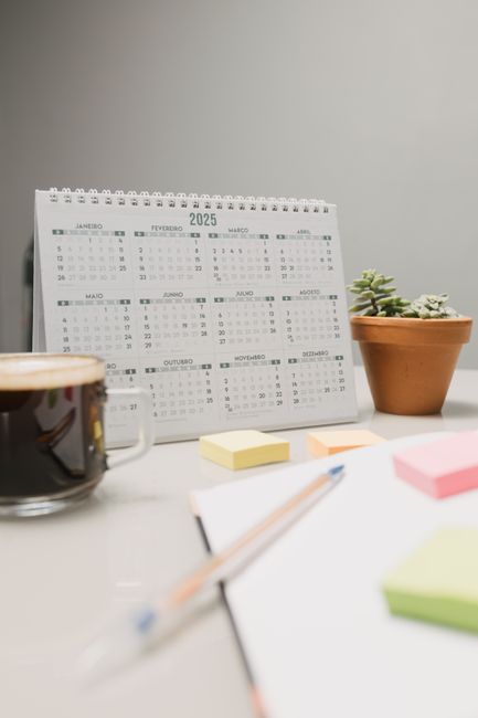 Simple desk setup featuring a 2025 calendar, potted plant, coffee, and sticky notes.