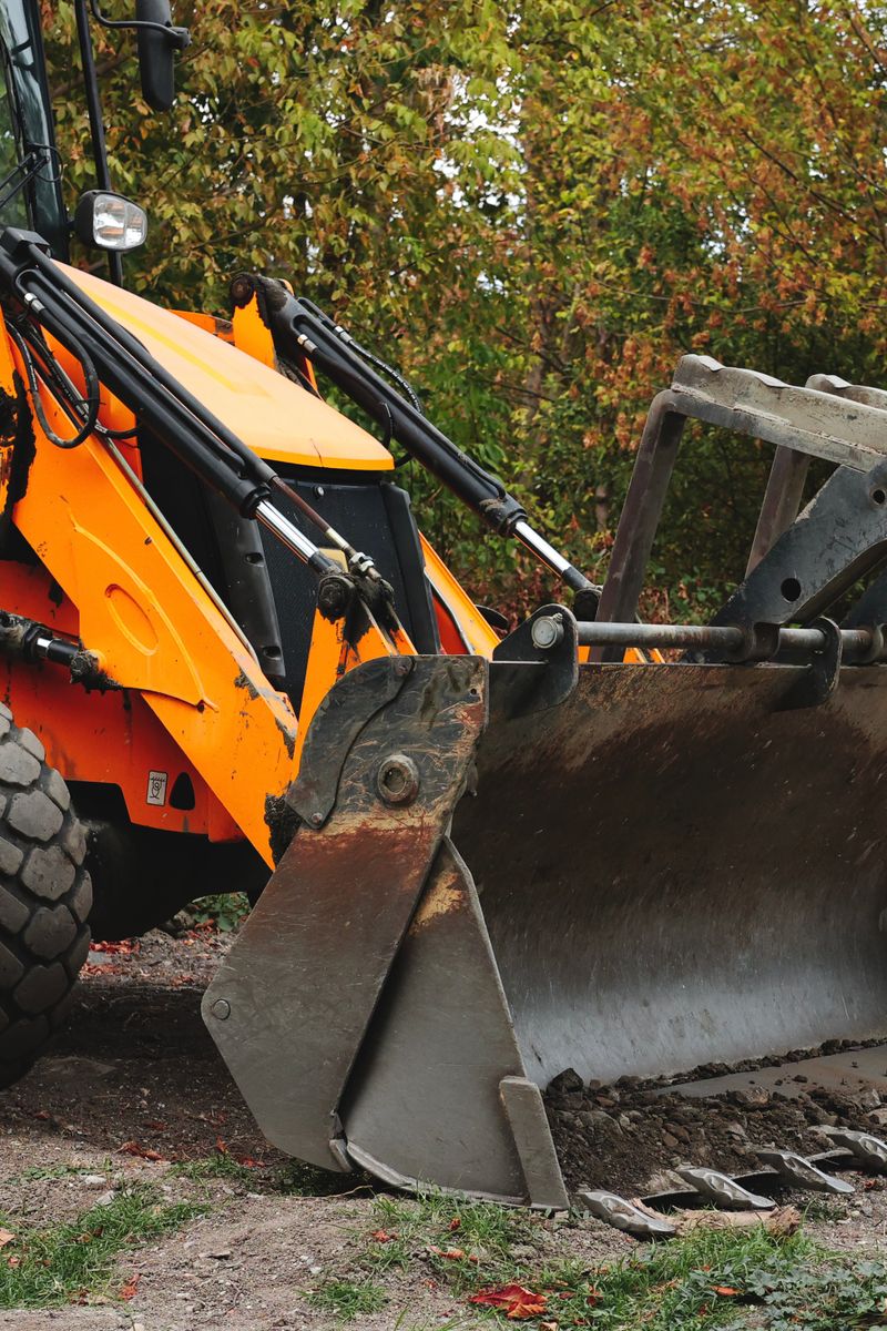 A brightly colored excavator machine parked on a worksite surrounded by autumn trees.